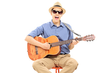 Young man with sunglasses and hat playing on acoustic guitar