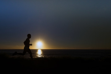 Silhouette of jogger along ocean horizon at sunset