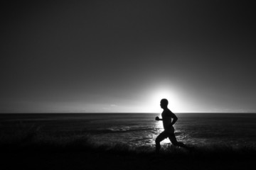 Naklejka premium Silhouette of jogger along ocean horizon at sunset