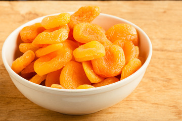 Bowl of dried apricots on wooden table background.