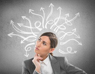 Serious, young businesswoman looking at many twisted arrows on t