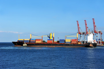 Tugboat assisting container cargo ship to harbor quayside