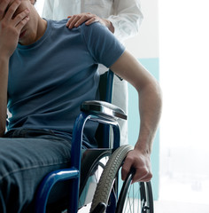 Doctor consoling young man sitting in wheelchair © stokkete
