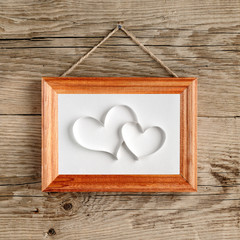 Two hearts in old picture frame hanging on wooden wall