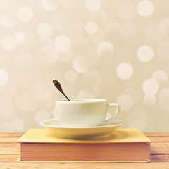 Coffee cup on book on wooden table over bokeh background