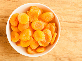 Bowl of dried apricots on wooden table background.