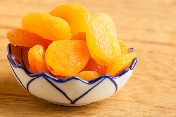 Bowl of dried apricots on wooden table background.