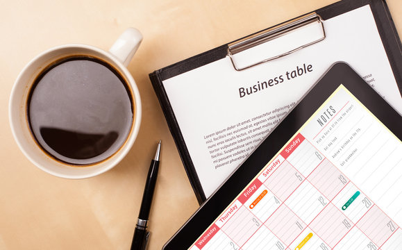 Tablet pc showing calendar on screen with a cup of coffee on a d