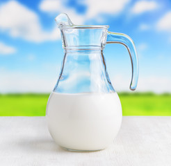 Jug of milk on meadow background. Half full pitcher