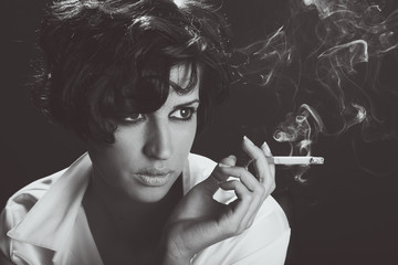 Elegant brunette woman smoking a cigarette on black background