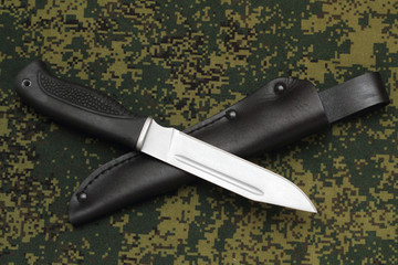 Military knife lying across leather sheath on  camouflage