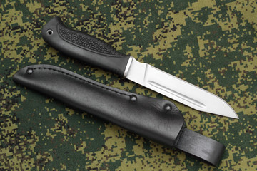 Military knife lying parallel with  leather sheath on camouflage