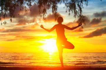 Fototapeta na wymiar Young woman silhouette practicing yoga on the beach at sunset.