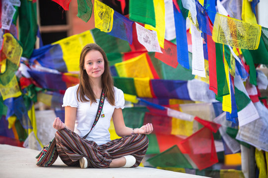 Teengirl sitting on Buddhist stupa, prayer flags flying