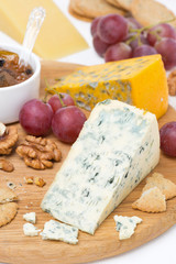 cheeses with mold, grapes, crackers, jam and nuts on a board