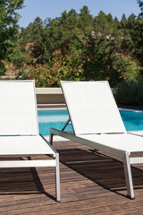 White loungers near a pool with trees in background