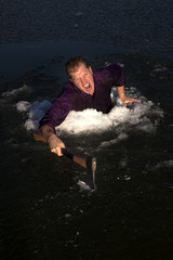 man in ice hole climbing out holding axe