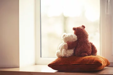 Fotobehang Two embracing teddy bear toys sitting on window-sill © AnnaElizabeth