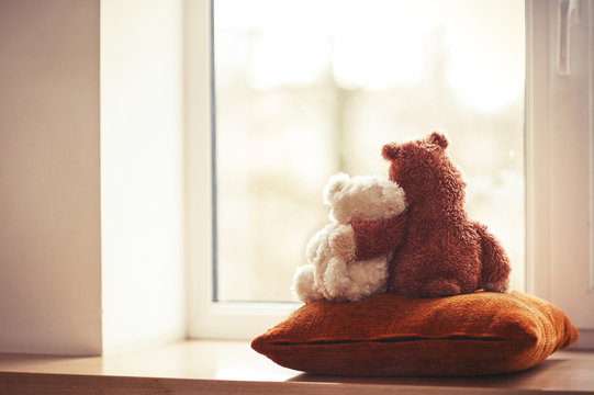 Naklejki Two embracing teddy bear toys sitting on window-sill