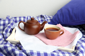 Cup and teapot on wooden tray on bed on wall background