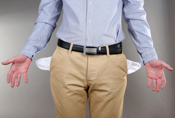 Man showing his empty pockets on grey background