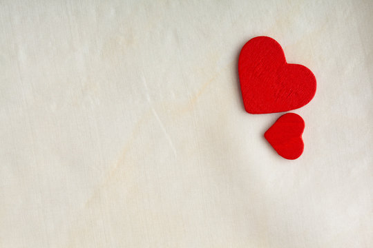 Red wooden decorative hearts on white cloth background.
