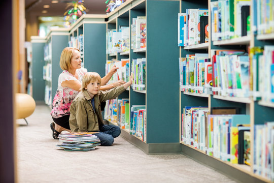Boy With Teacher Selecting Books From Bookshelf