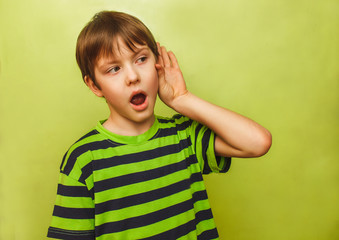 baby teenager boy listens to put a hand his ear on green