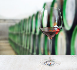 Glass of wine and wooden barrels in winery