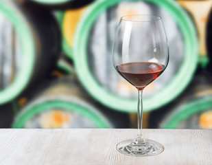 Glass of wine and wooden barrels in winery