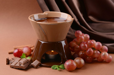 Chocolate fondue with fruits, on  brown background