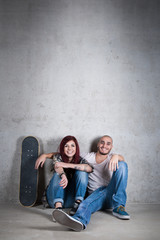 Naklejka premium Happy couple portrait sit on the ground with skateboard against
