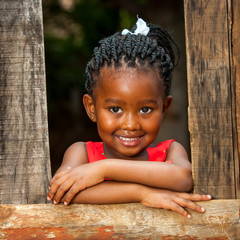 Little african girl leaning on wooden fence.
