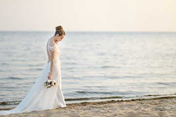 Fototapeta na wymiar Bride walking along sea coast on sunset