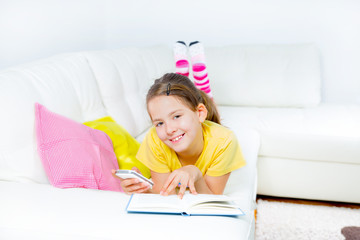 Naklejka premium little girl with smart phone and book at home