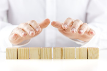 Man holding protective hands above eight wooden cubes