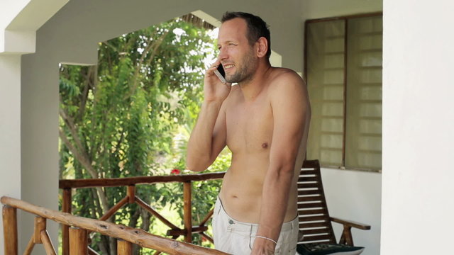 Happy shirtless man talking on cellphone on country house porch