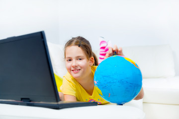 cute little girl on a sofa with a laptop and globe