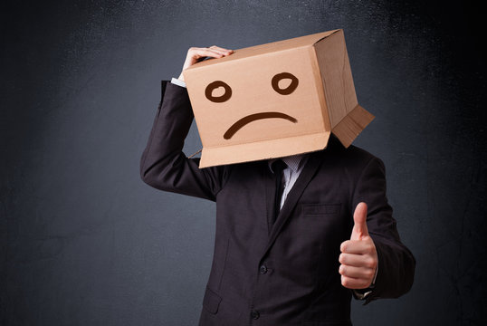 Businessman gesturing with cardboard box on his head with sad fa