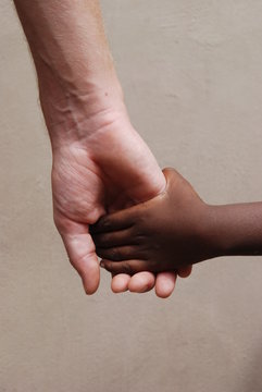 arbige Kinderhand h&auml;lt weisse Erwachsenen Hand