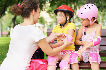 Young woman helping to put on elbow pads two girls © Pavel Losevsky