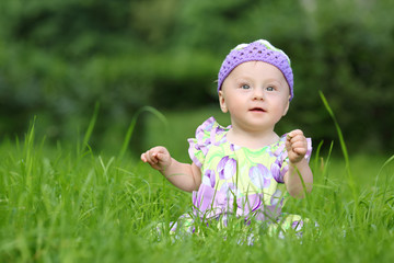 Little girl in a knitted hat sitting on fresh grass