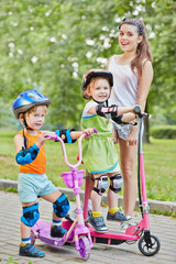 Teenage girl and two little children on scooters in park