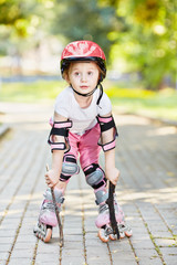 Little girl in protective equipment and rollers stands on park