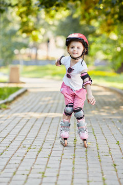 Little girl in protective equipment roller-skates on walkway