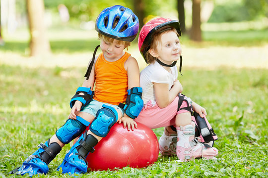 Little boy and girl in roller equipment sit together on red ball