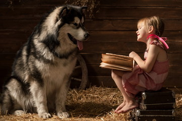 Little girl reading a book to his dog in the barn