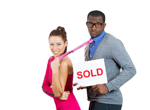 Closeup portrait young couple, businesspeople, female woman happy have male man hands tied up with rope, giving thumbs up, guy holding sold sign, isolated white background. Emotion facial expression