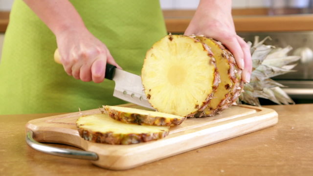 Woman's hands cutting fresh pineapple on kitchen