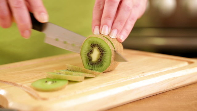 Woman's hands cutting fresh kiwi on kitchen